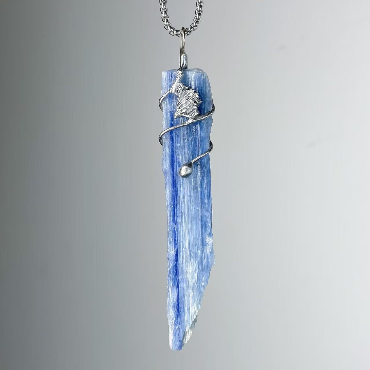 Handmade blue kyanite crystal pendant with ocean wave-inspired tin wrap